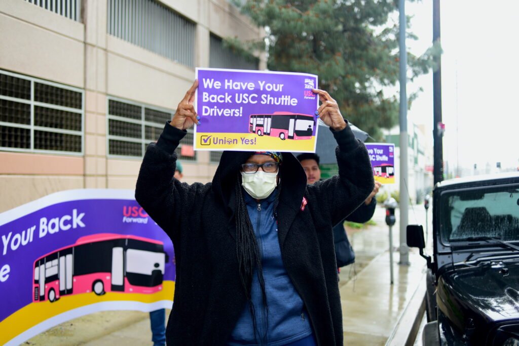 SEIU 721 member holds "We have your back USC Shuttle Drivers" sign on the street.