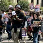 Occidental students marching through campus holding signs. Student in the center of the photo is wearing a black shirt and clapping.